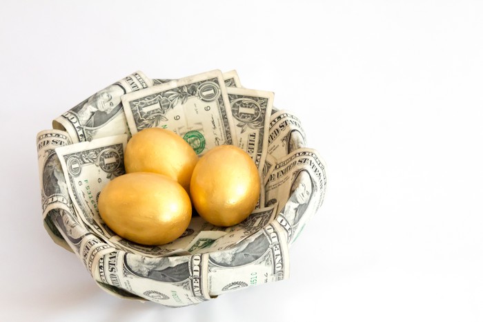 A basket of dollar bills filled with three golden eggs. 