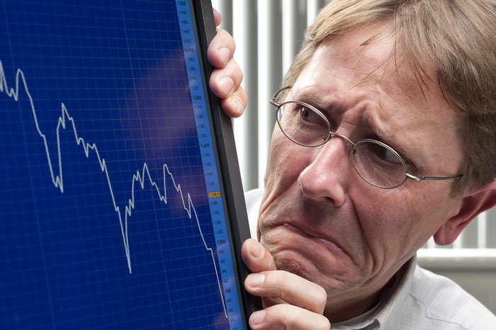 A visibly worried investor looking at a plunging chart on his computer monitor.