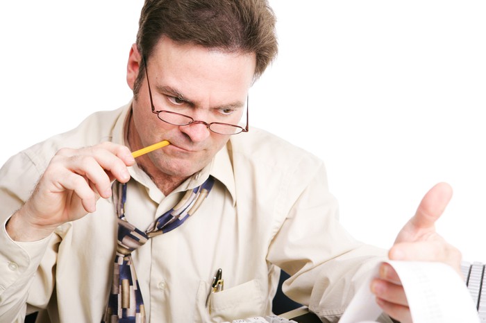 An accountant biting a pencil as he looks over printed figures from his calculator. 