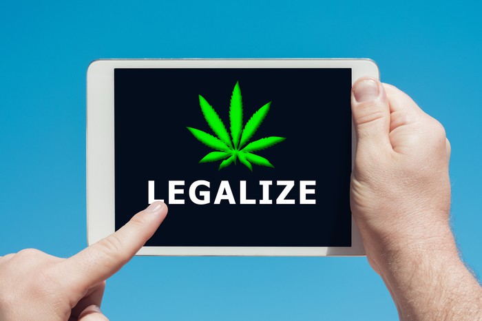 A person holding and touching the screen of a tablet that shows a cannabis leaf with the word legalize underneath. 